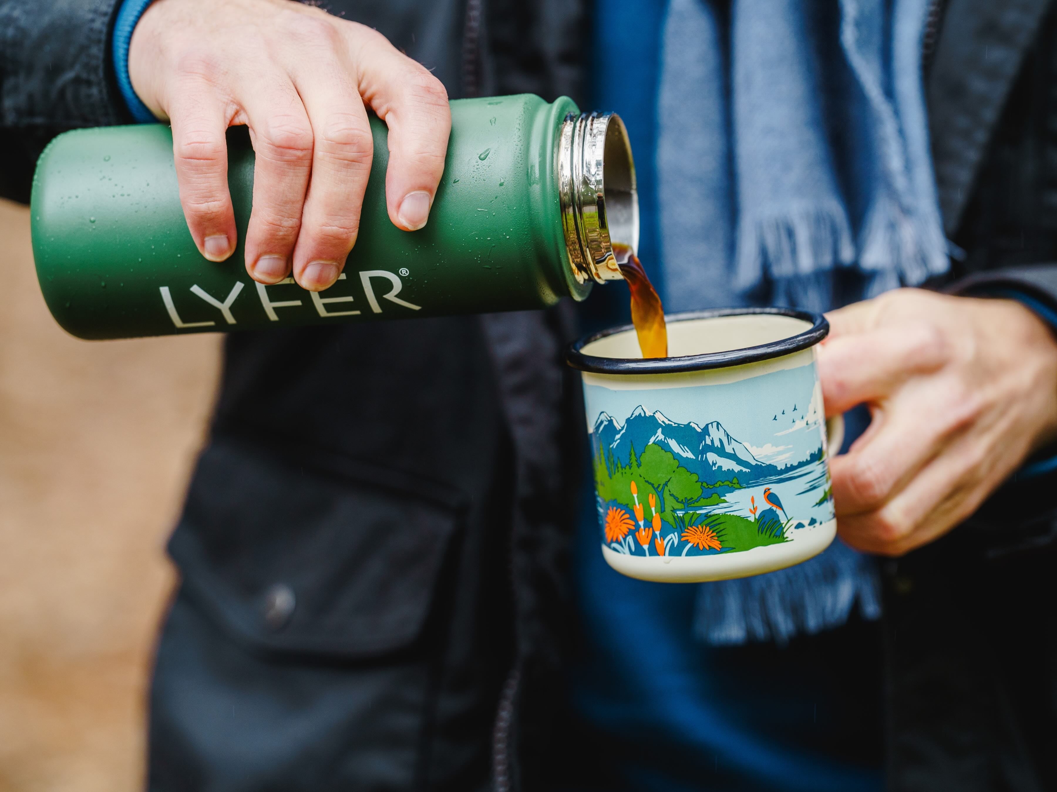 Image of model pouring coffee out of Lyfer Thermo Bottle into a Lyfer Field Mug out in nature.