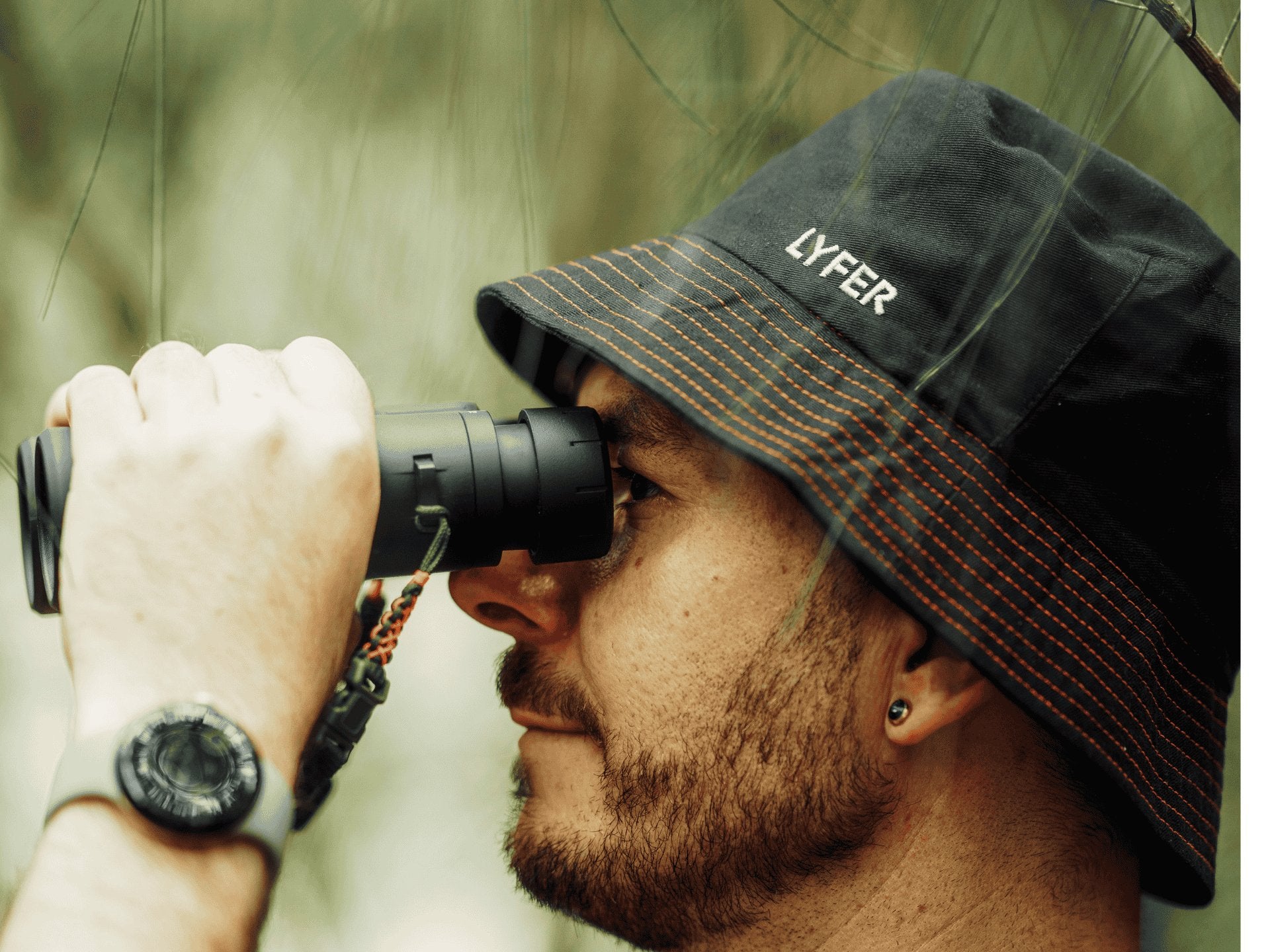 Model wearing LYFER bucket hat outdoors looking through binoculars