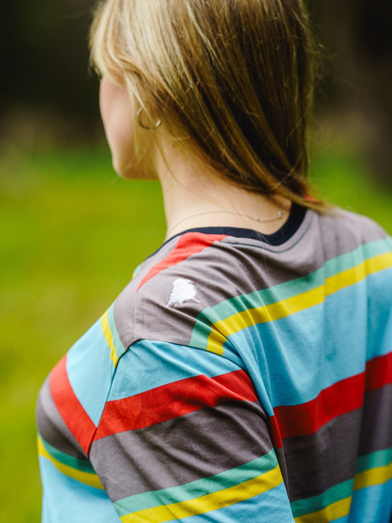 Model wearing the Endangered range t-shirt with a focus on the hand sewn birdmark logo on shouldered wit the tshirt showing the colours of the golden-shouldered parrot.