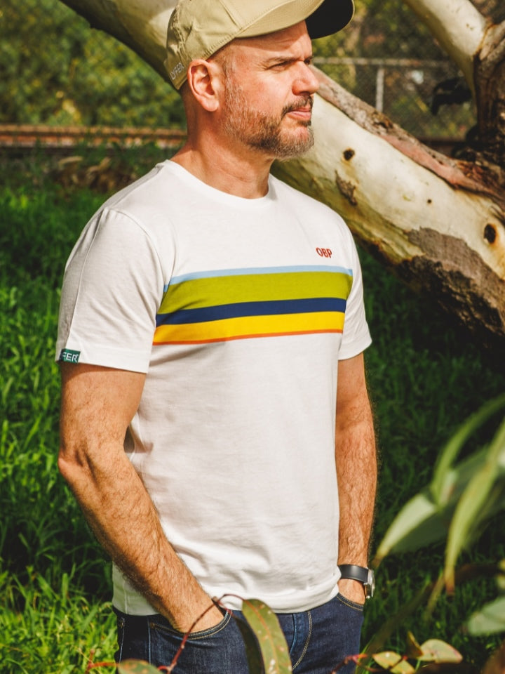 Model wearing the LYFER Orange Bellied Parrot tshirt, standing in a park wearing a cap