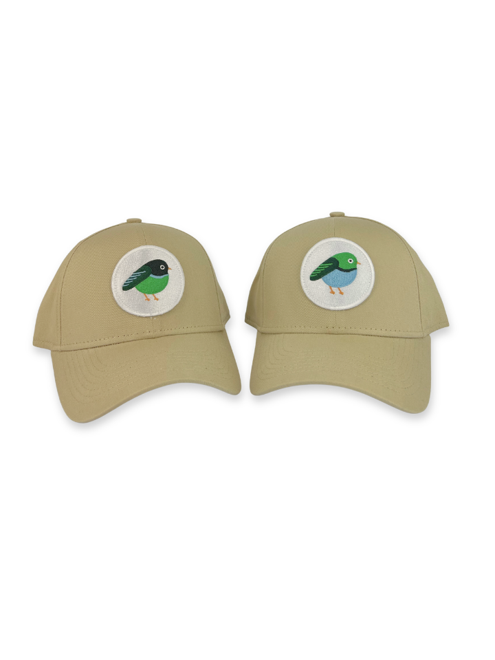 Two khaki baseball caps shown side by side on a white background, each featuring a circular embroidered bird patch on the front panels.