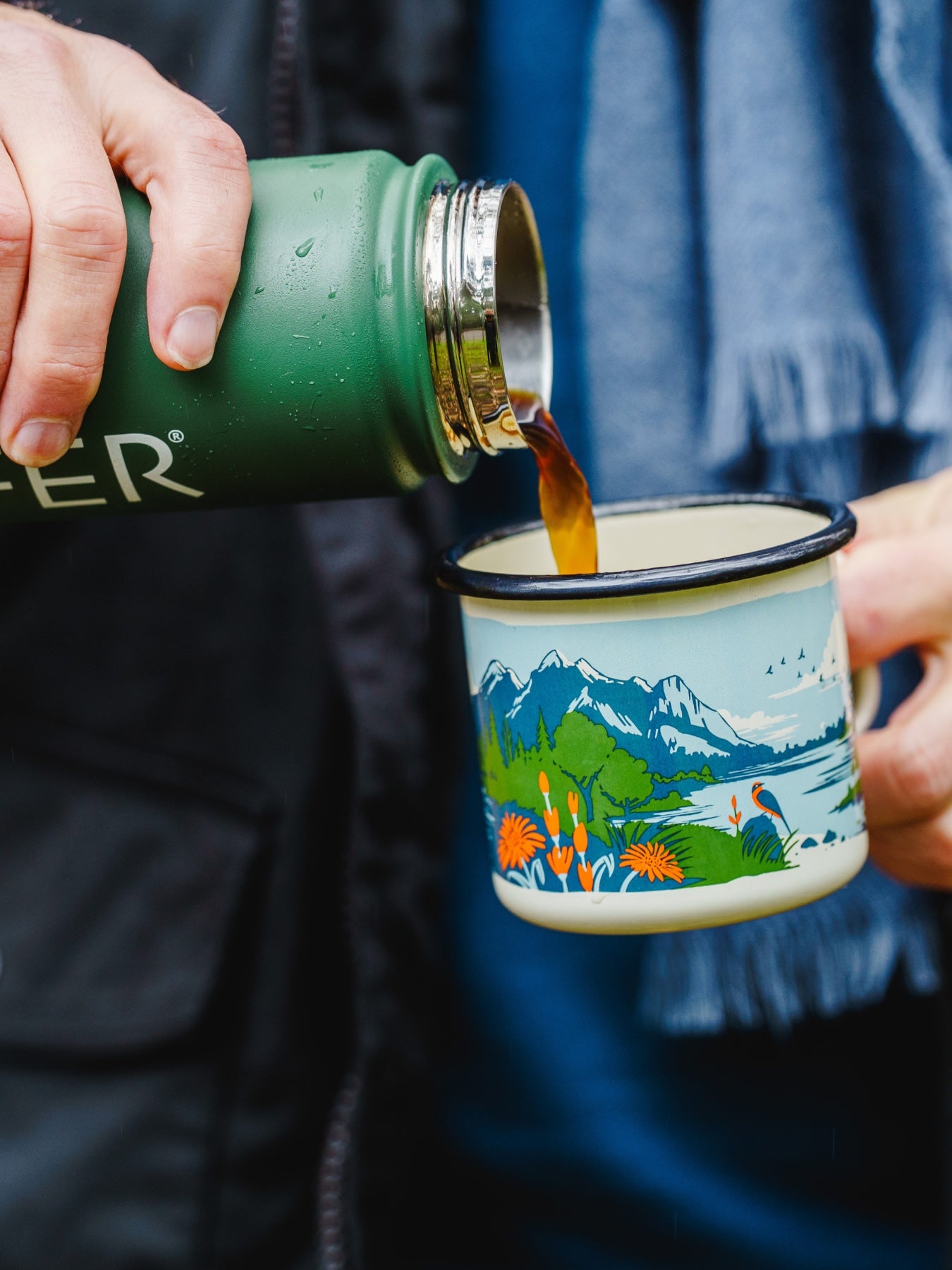 Person pouring liquid from the LYFER green thermos into a LYFER enamel mug with a hand drawn design.