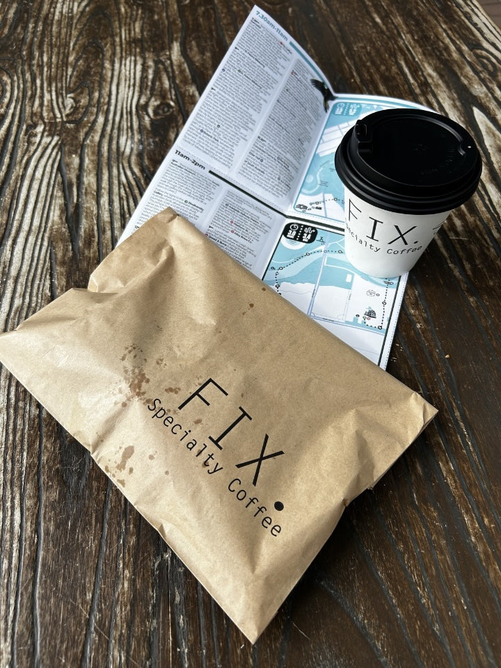 Brown paper bag with 'FIX Specialty Coffee' branding, a coffee cup, and a map on a wooden surface.