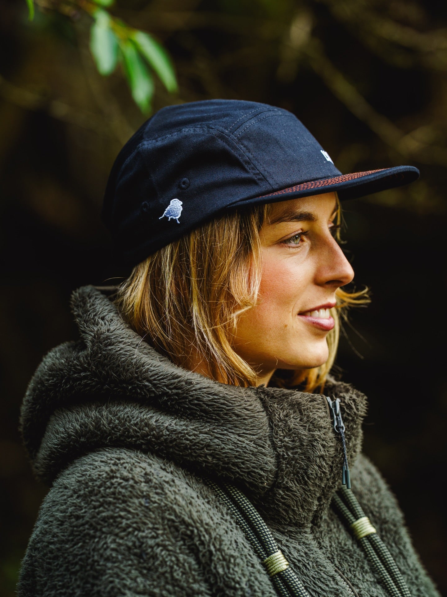 Model wearing Lyfer 5 panel cap with birdmark logo on side while in nature.