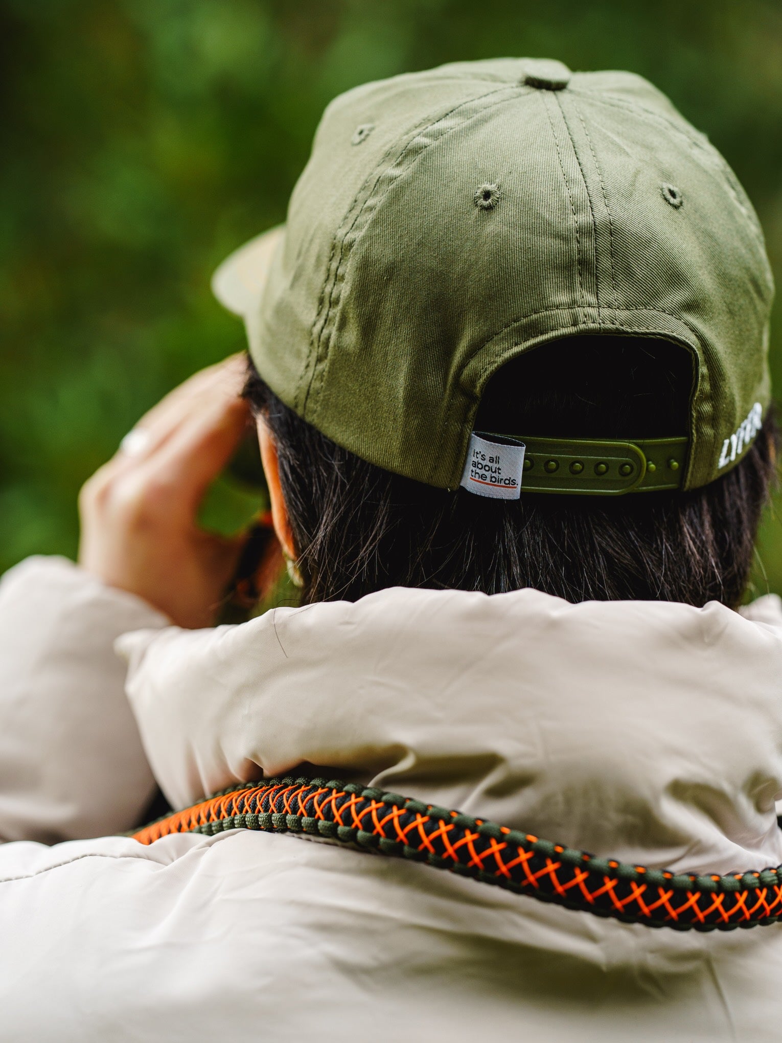 Person wearing a Lyfer green Birmark 6 panel cap, highlighting the It's all about the birds slogan woven tag on the back of the hat.