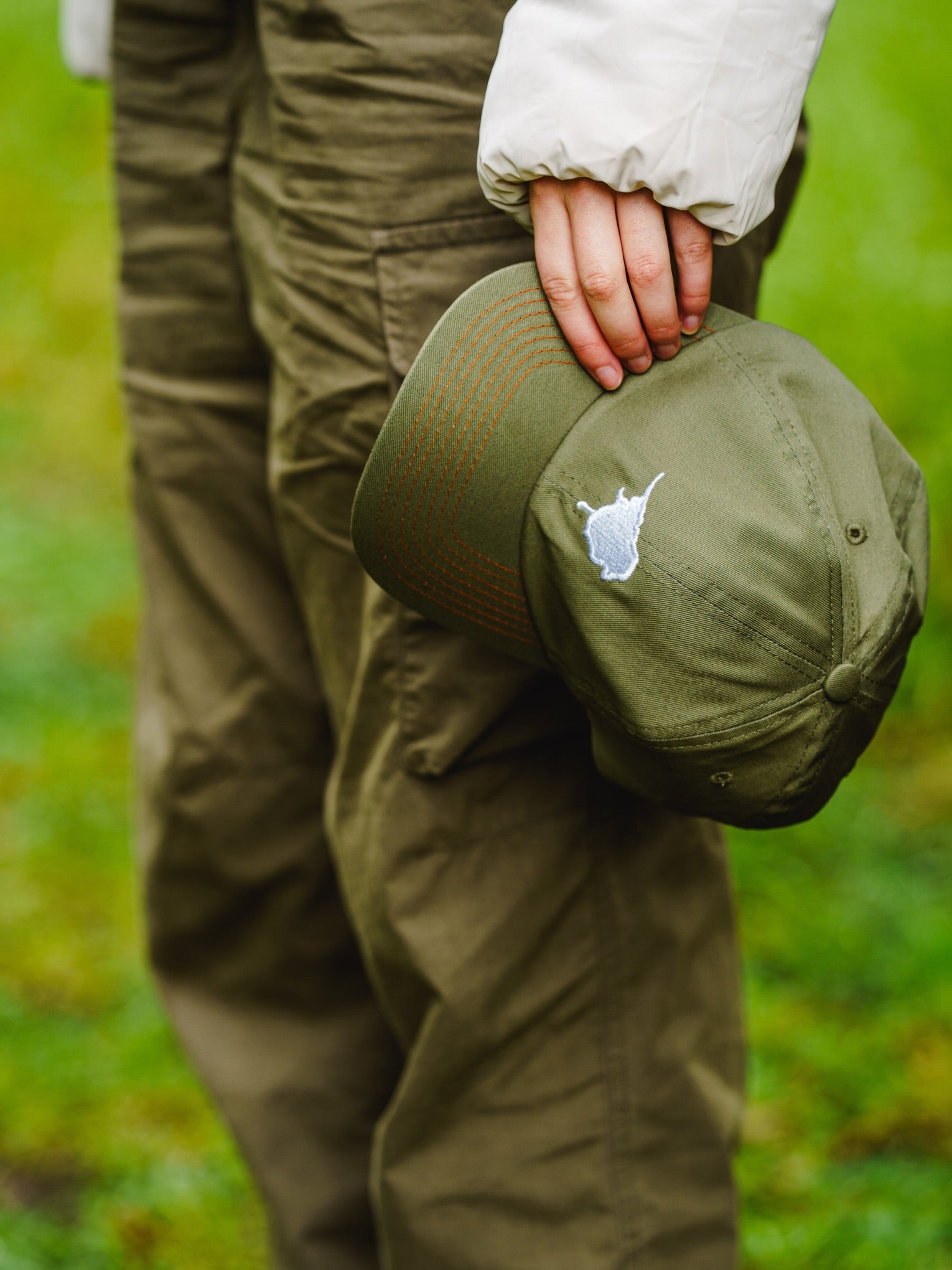 Person holding a Lyfer green birdmark 6 panel cap while out on a bird walk.