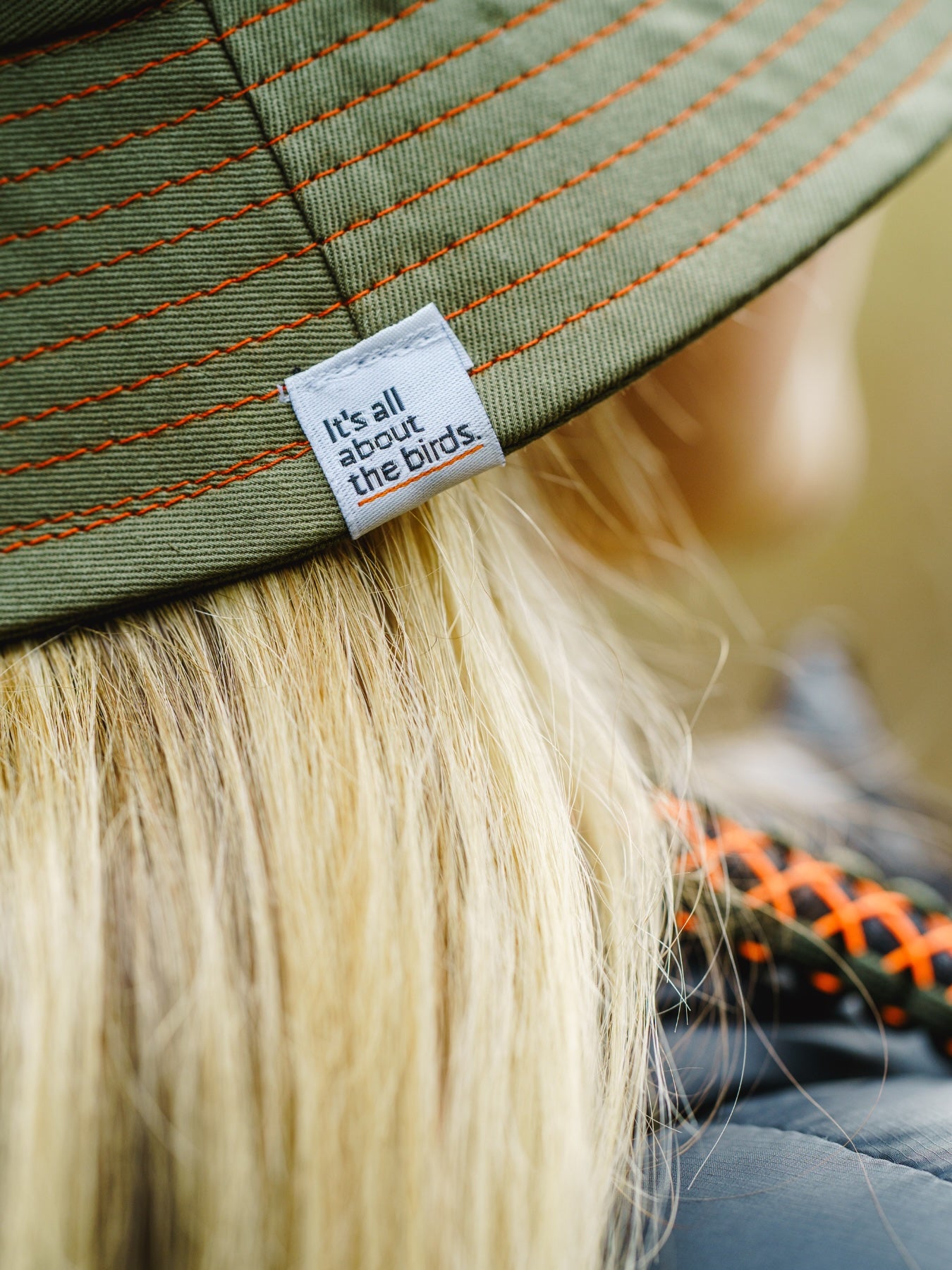 close up of model wearing the lyfer birdmark bucket hat our in nature birding, showing the Its all about the birds wove tag and detail.