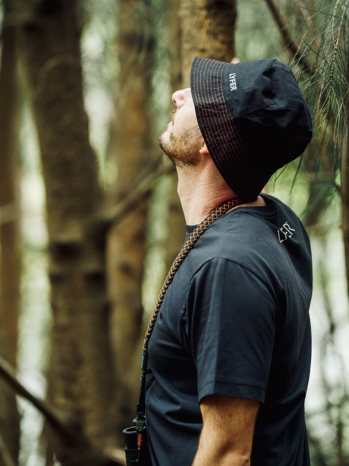 Lyfer Brand Bucket Hat in Black worn by model out in nature, it is a sustainably
and ethically made birdwatching hat that is a great gift for birder in Australia.