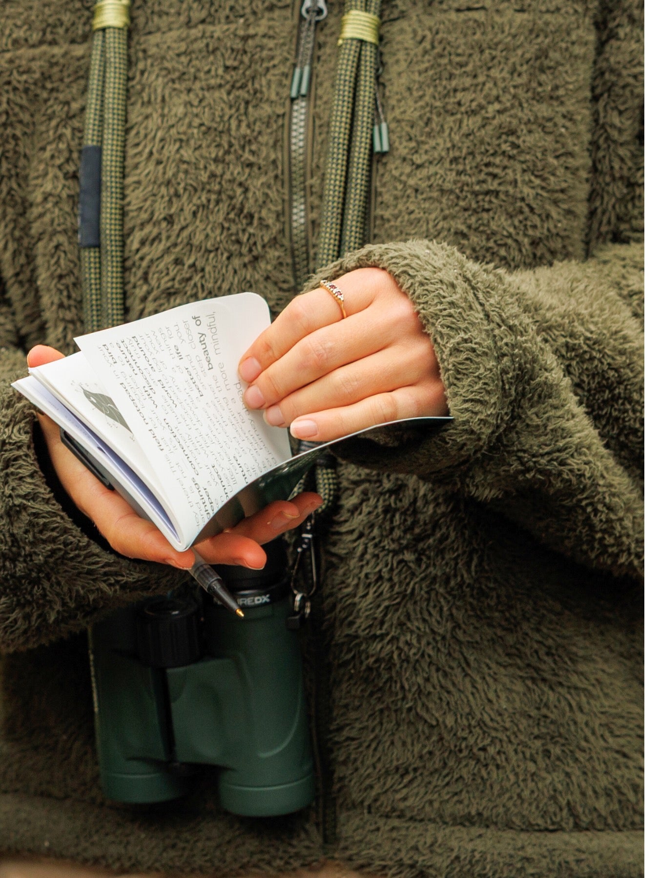 Person holding a Lyfer field notepad with binoculars in a green jacket