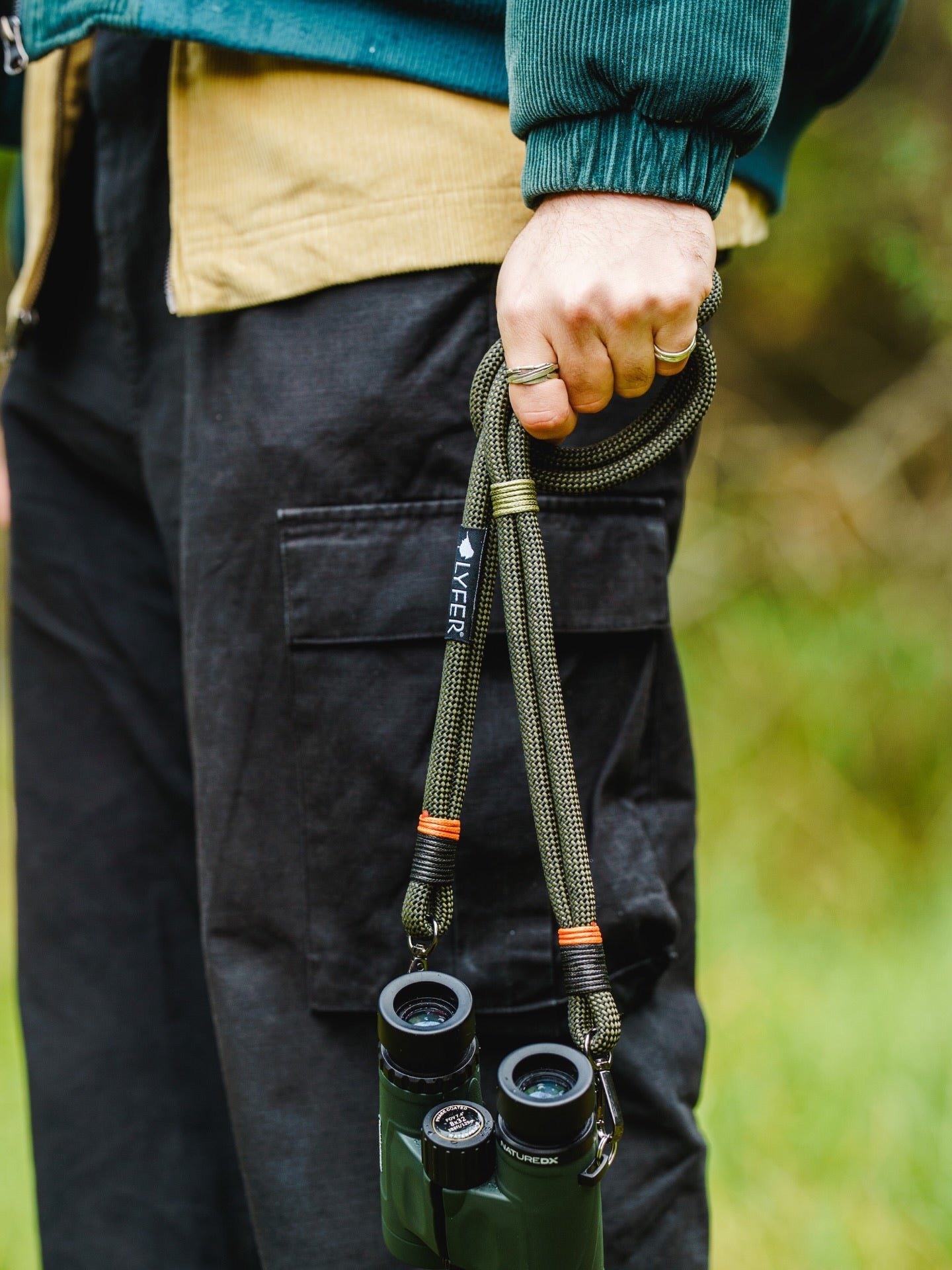 Model holding Lyfer original binocular straps out in nature while bird-watching.