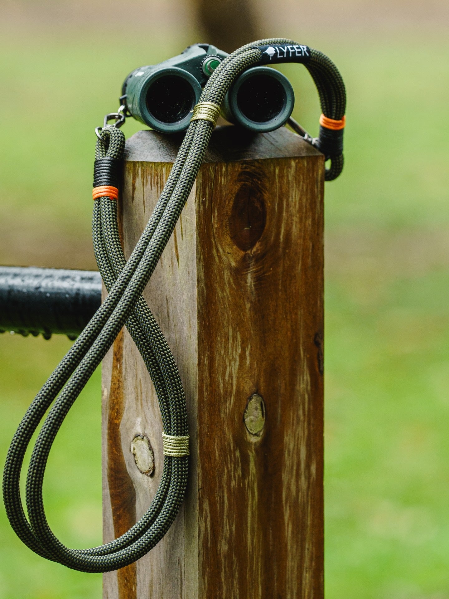 Close up of Lyfer original binocular and camera straps attached to binoculars placed on a wooden fence.