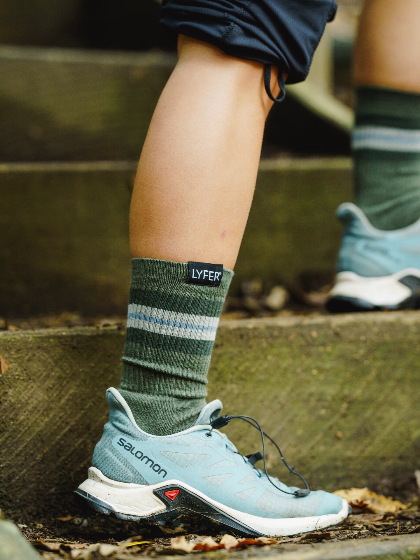 Bird watcher wearing Lyfer Field Original socks with a visible LYFER brand label and blue Salomon shoes on outdoor steps.