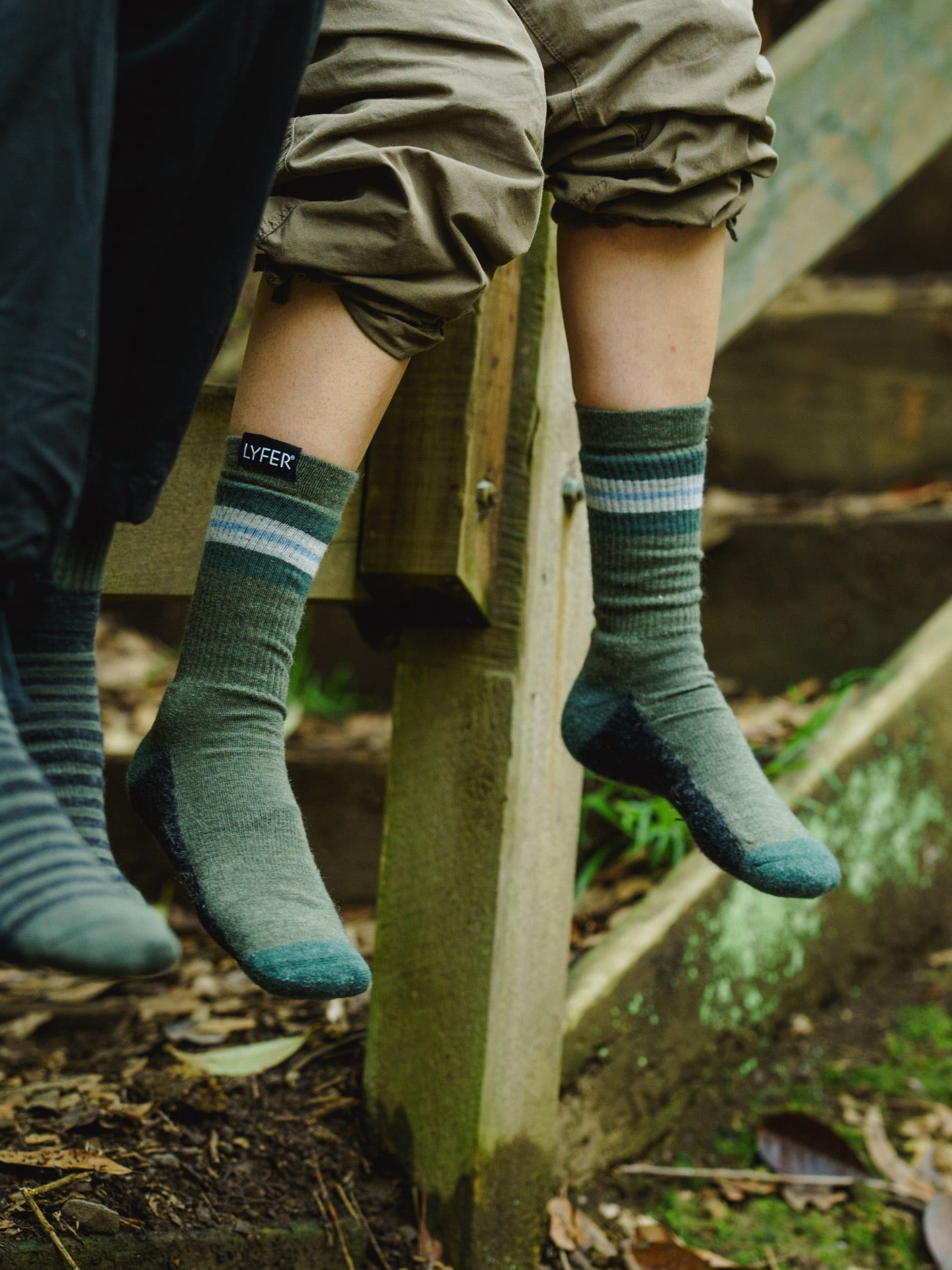 Two birders wearing Lyfer Original Field Socks with a the LYFER brand woven tag logo, sitting on wooden steps outdoors.