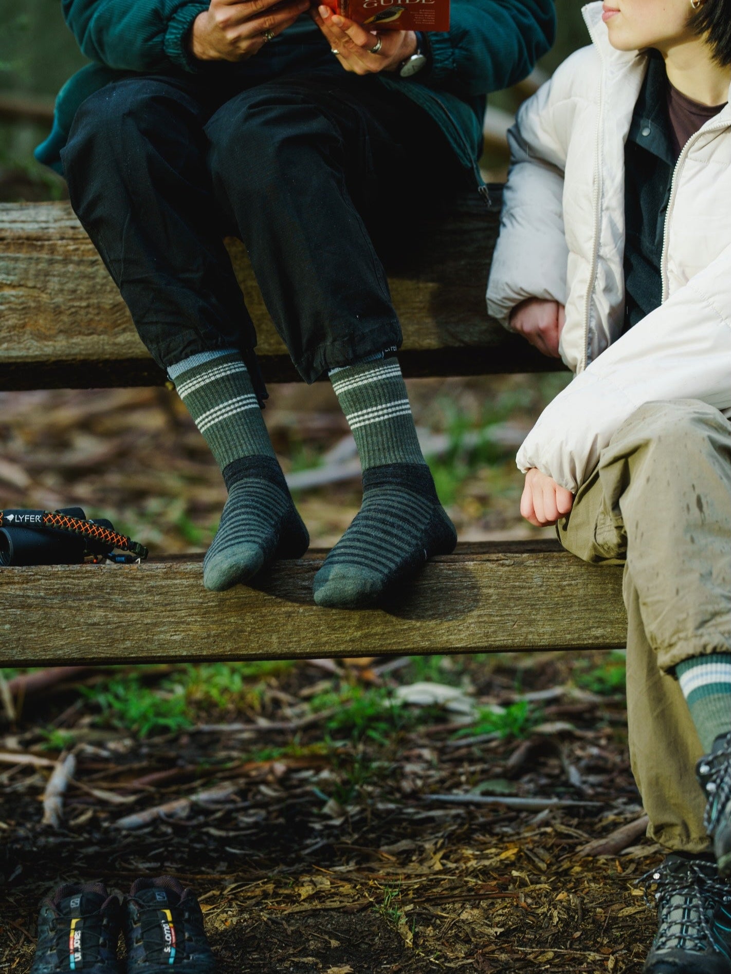 Two people sitting on a wooden bench outdoors while bird watching, wearing Lyfer original socks.