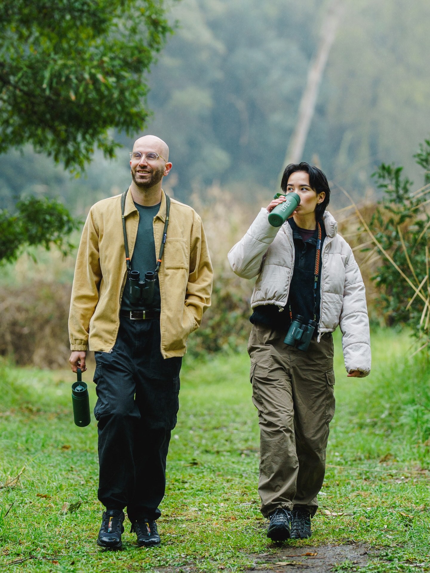 Two people walking outdoors in a natural while birdwatching, holding lyfer thermo bottles.