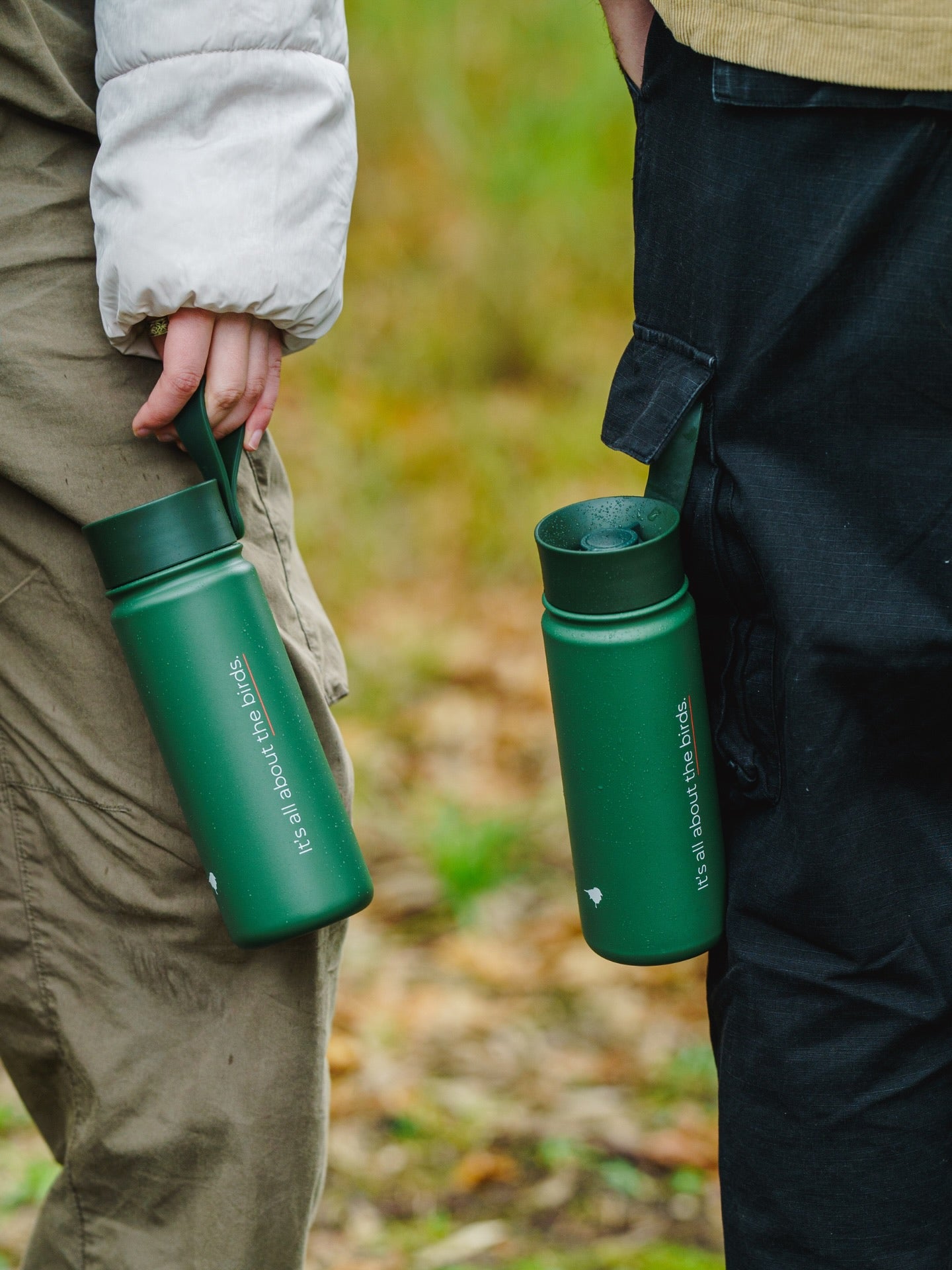close up of Lyfer thermo bottle held by people in outdoor clothing with a blurred natural background, showing detail of bottle.