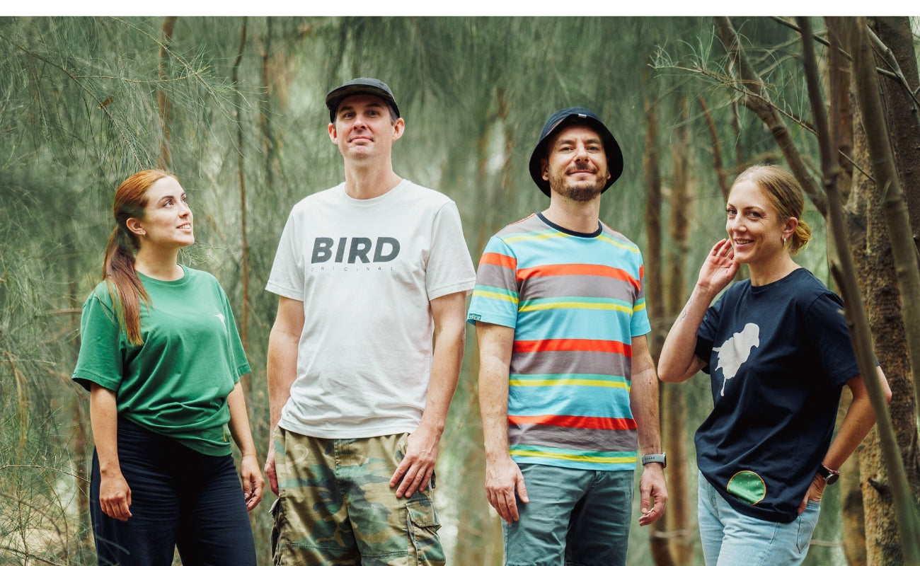 Four birders standing in a forest, with one wearing a 'BIRD' shirt, showing the tshirt range of the lyfer tshirts