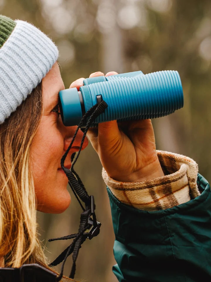 Close up shot of femail model holding NOCS binoculars 8x32 in blue, while out in nature looking at birds.