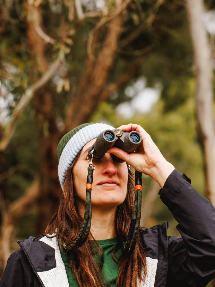 Model outdoors with a beanie, looking through binoculars with straps