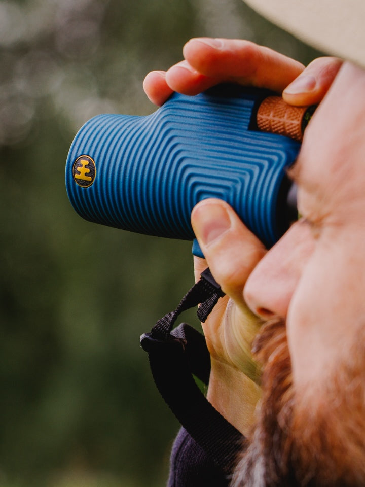 Person holding a NOCS blue monocular with a blurred natural background