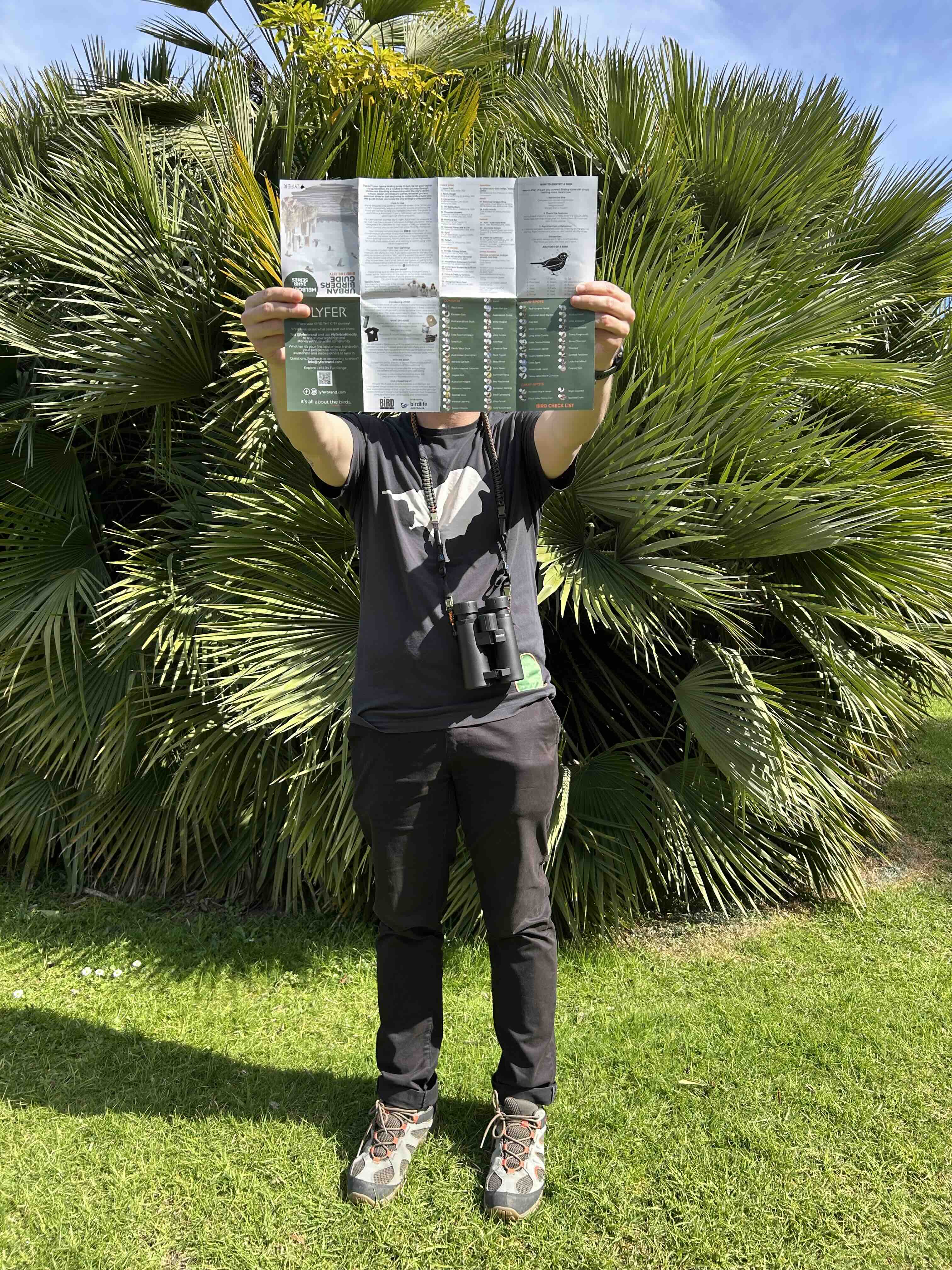 Person holding a birding map of melbourne in front of their face with palm trees in the background