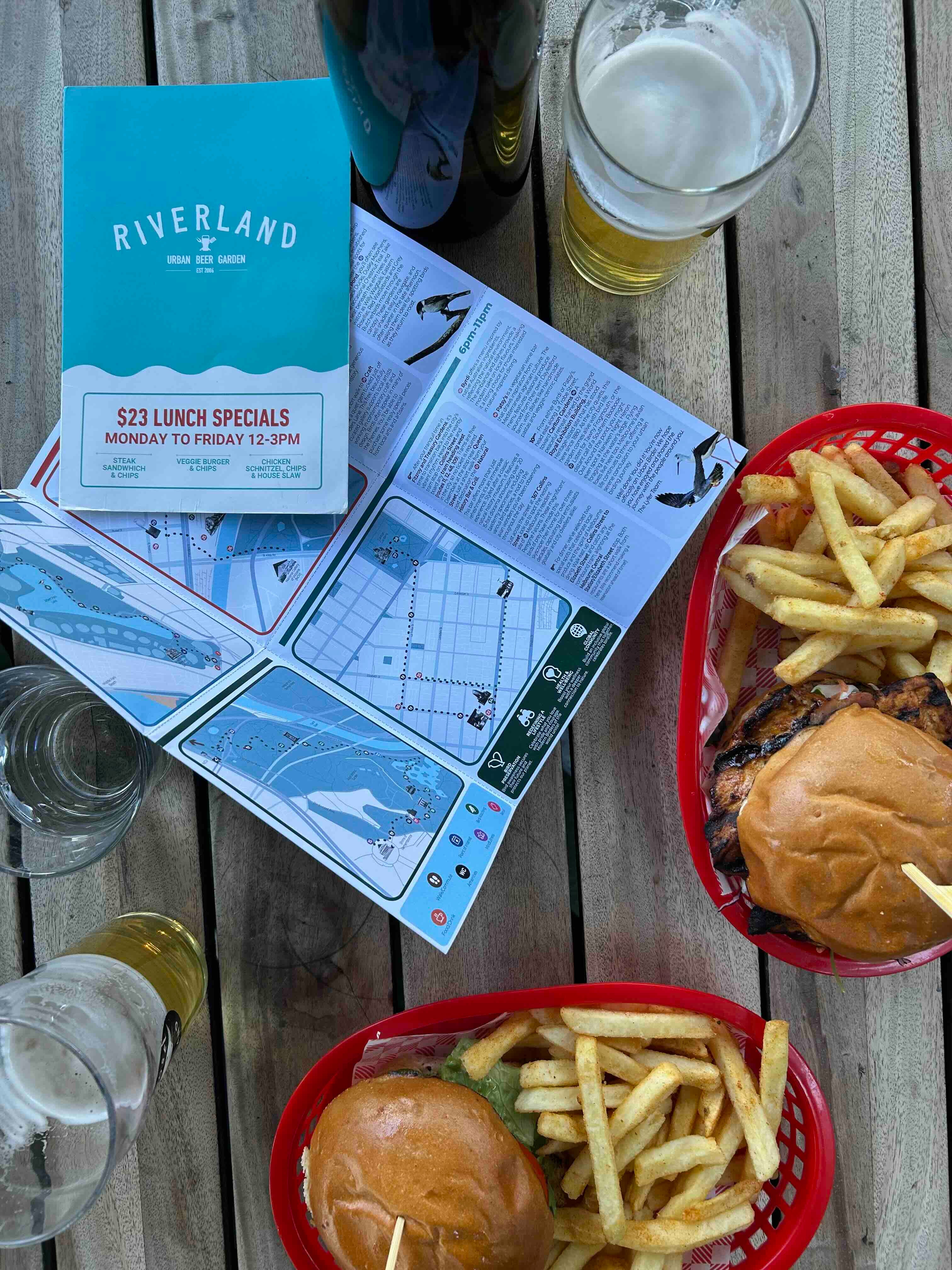 Outdoor dining setup with burgers, fries, drinks, and a menu on a wooden table along with the Lyfer birding guide of melbourne