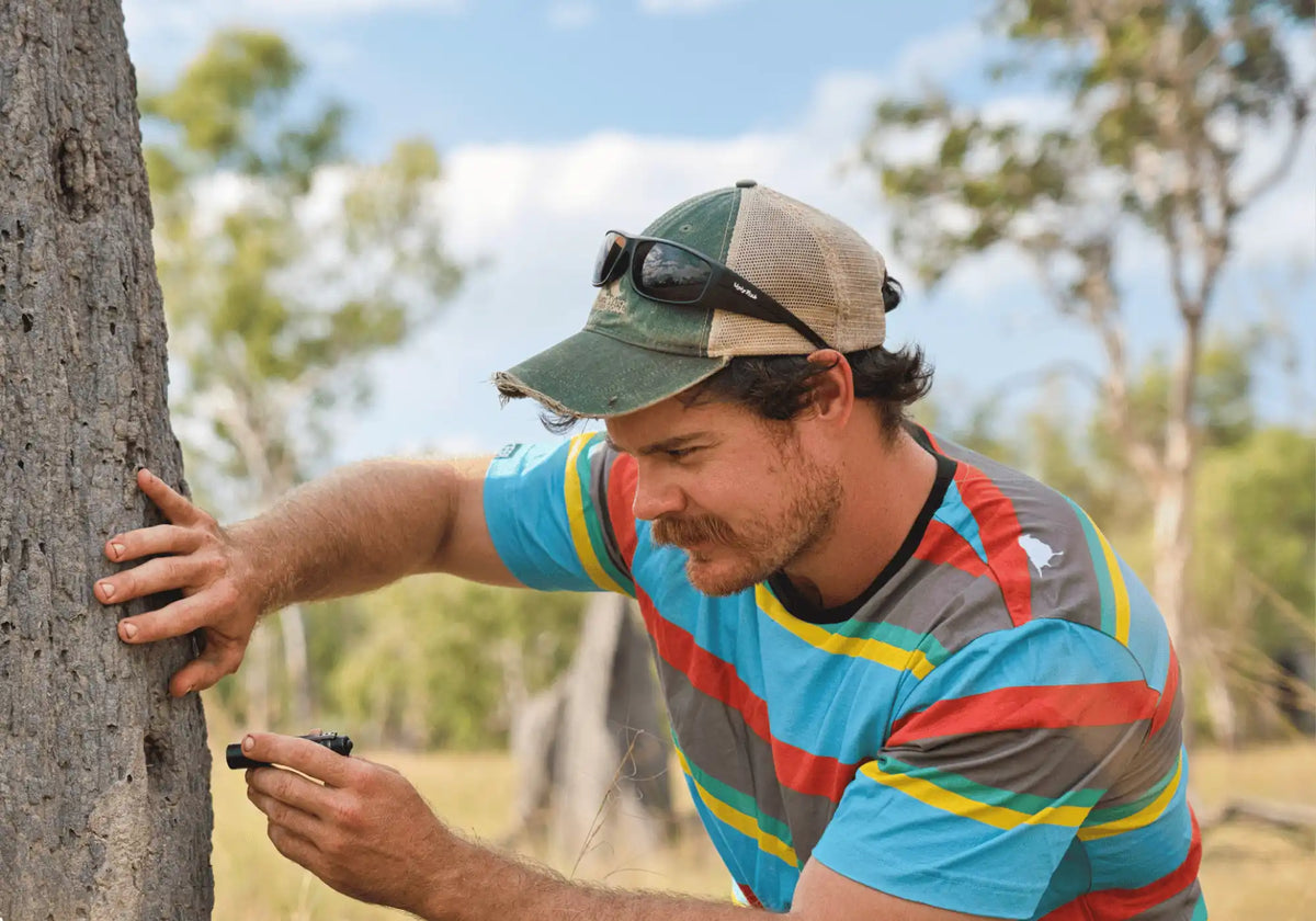 Image of model wearing an Endangerd Range Lyfer team for the Golden-shouldered Parrot, leaning against a tree.