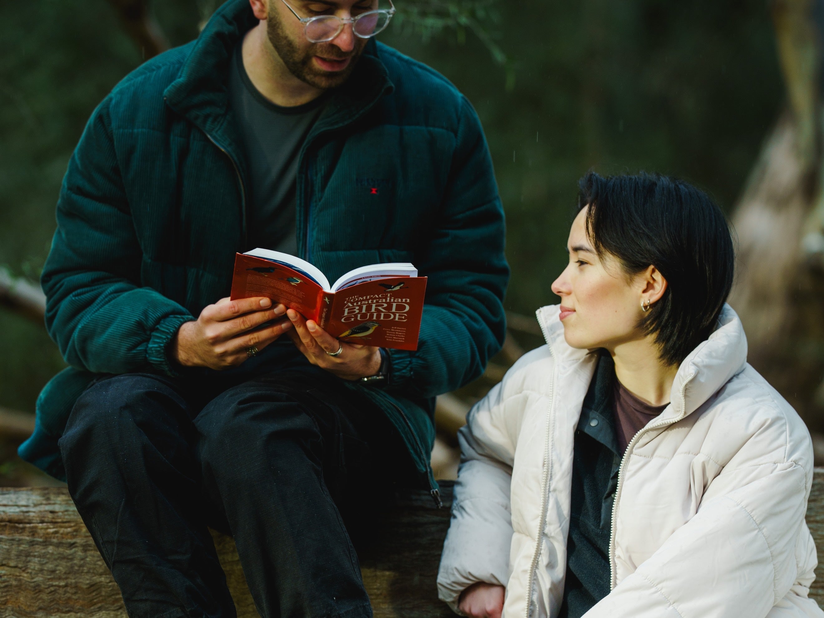 Image of birders sitting on a bench outdoors reading the Compact Bird Guide by CSIRO publishing