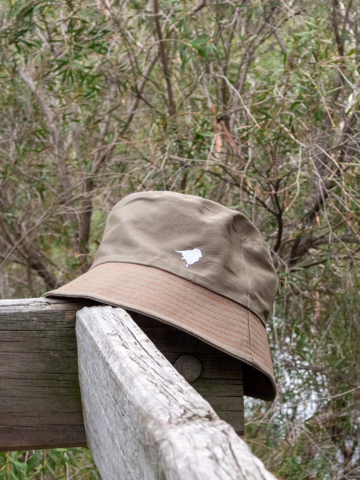 Lyfer Green Bucket Hat perched on the side of a wooden outdoor balustrade