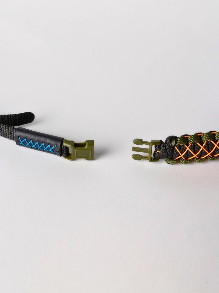 Two paracord wristlets or lanyard-style accessories shown on a plain light background. One is black with bright blue zigzag stitching and an olive green buckle.