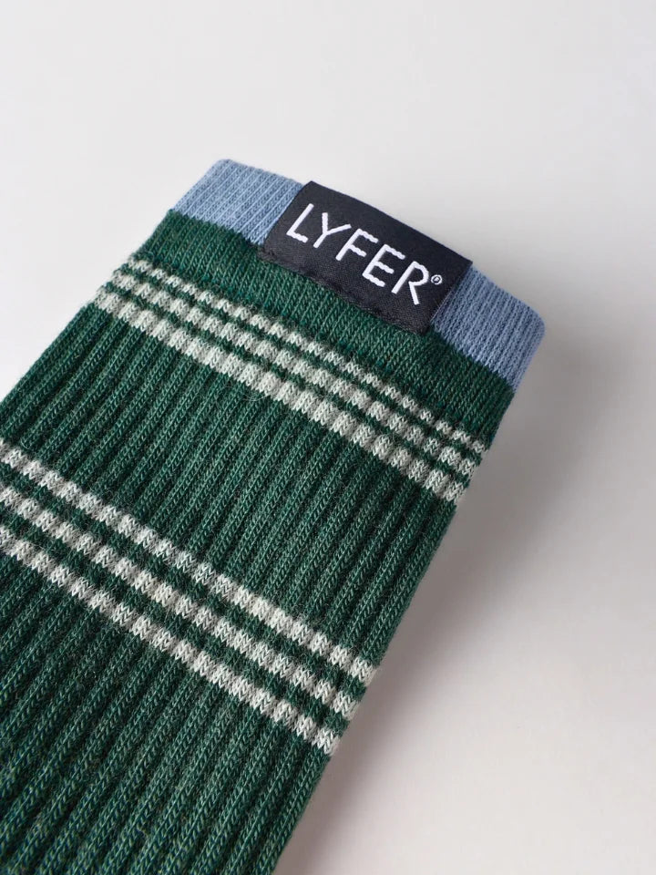 A close-up of a ribbed knit sock in dark green with white and light blue stripes, featuring a black fabric brand label that reads 'LYFER'.