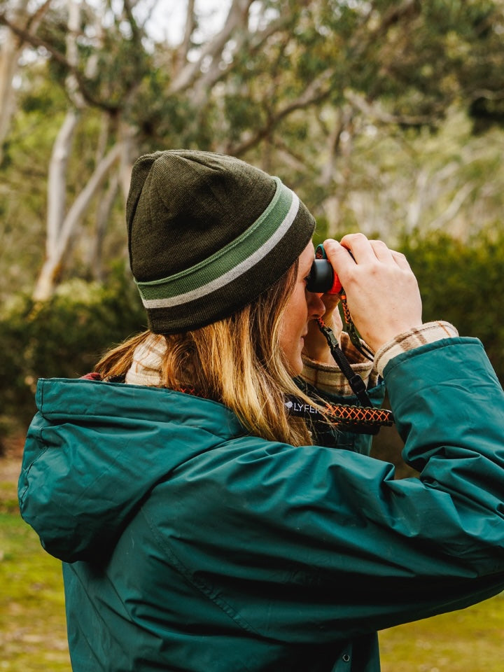 Female model wearing the LYFER Jersey knit Merino wool hat, outdoors with binoculars.