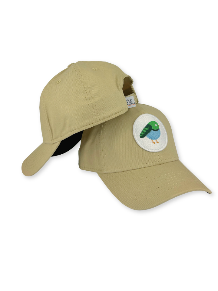 A khaki baseball cap with a curved brim, featuring a circular embroidered patch of a green and blue bird on the front. The cap is shown from a three-quarter angle against a plain white background.