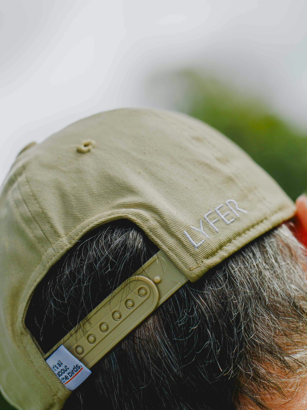 Image of back of models head wearing a LYFER cap with LYFER embroidery and Its all about the birds sewn in tag