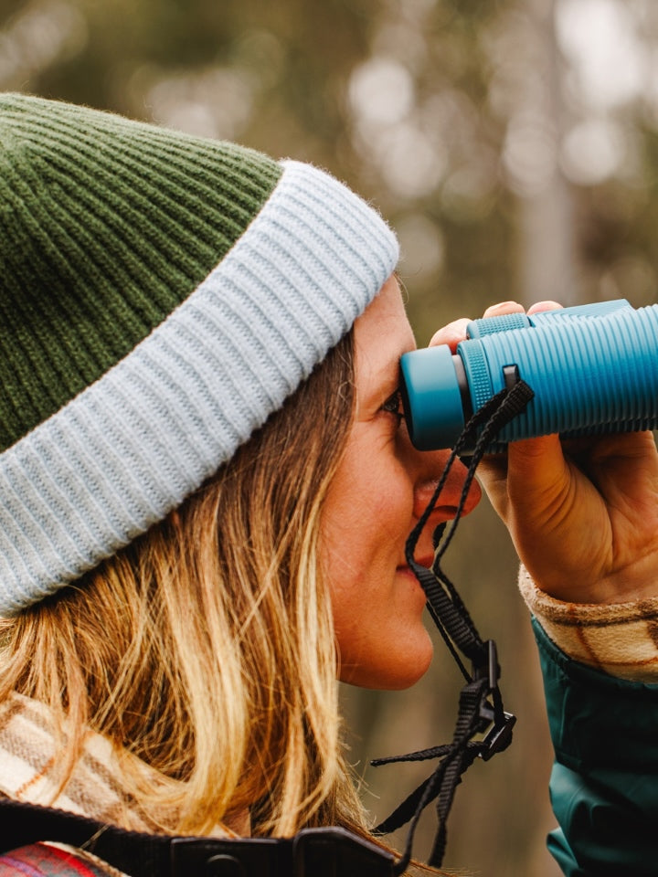 Close up of model wearing LYFER ribbed knit beanie texture, holding a pair of binoculars outdoors