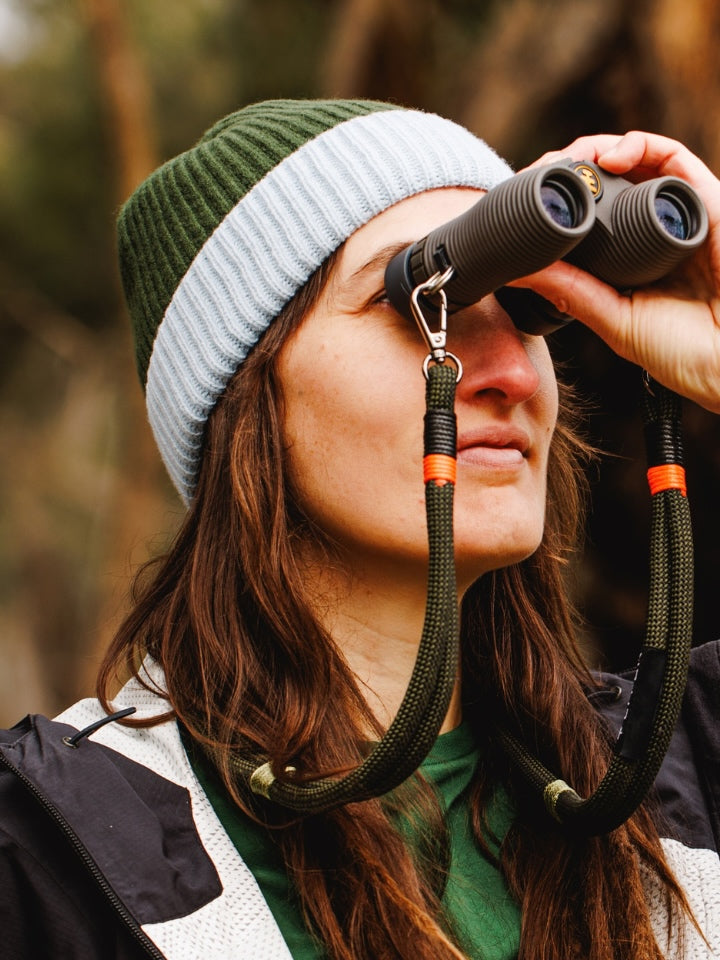 Female model wearing a LYFER ribbed knit beanie holding a pair of NOCS binoculars
