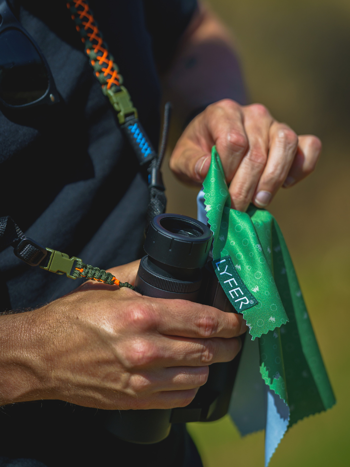 Close up Binocular and camera cleaning cloth, binoculars being cleaned with bino straps in background