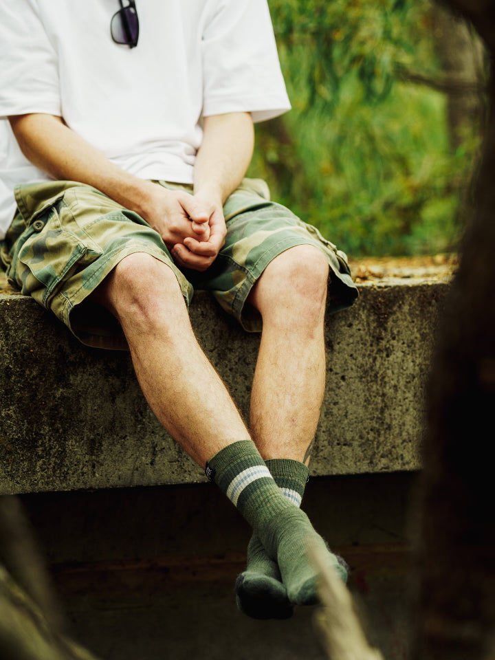 Image of model sitting in nature wearing Lyfer Original Field Socks.