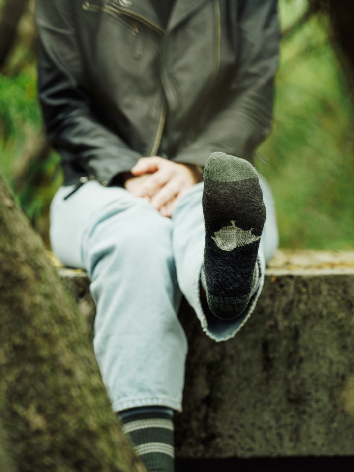 Model lifting foot to show Lyfer birdmark logo on the sole of the sock.