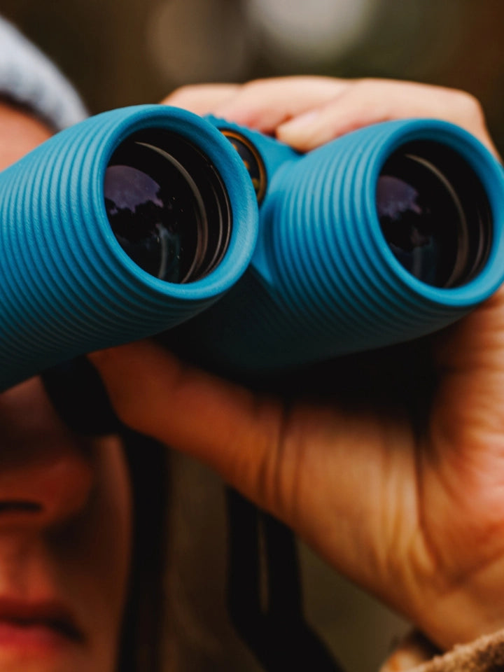 Close up shot of model holding NOCS binoculars 8x32 in blue, while out in nature looking at birds.