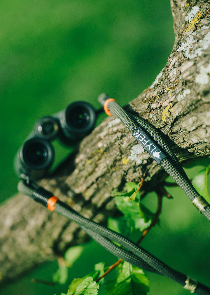 Lifestyle shot  Lyfer's birding binocular & camera straps, showing the woven tag, thread detail and carabiner fastening clips. 