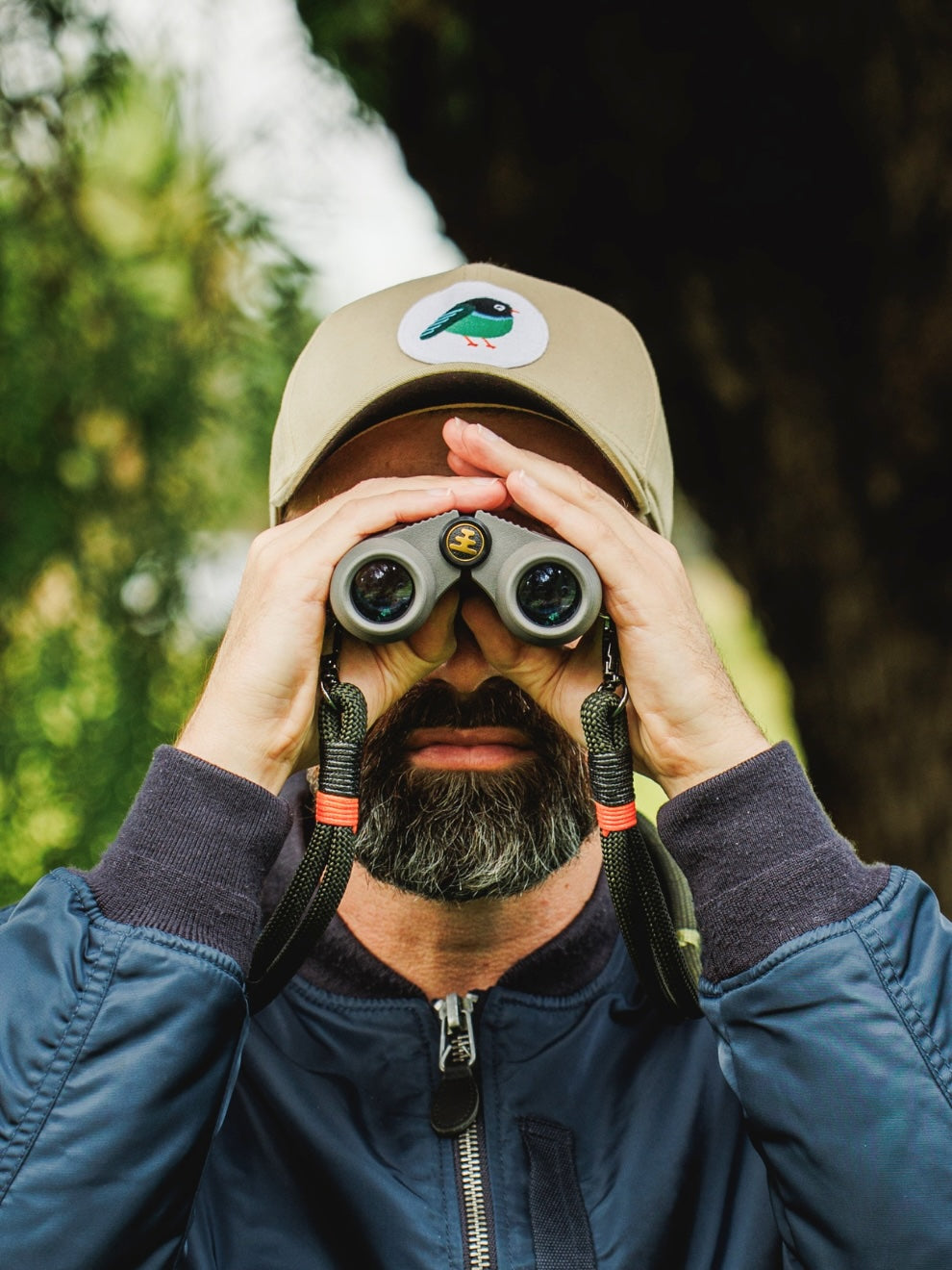 Bird-watching outdoors wearing a LYFER Patch cap with Nocs binoculars