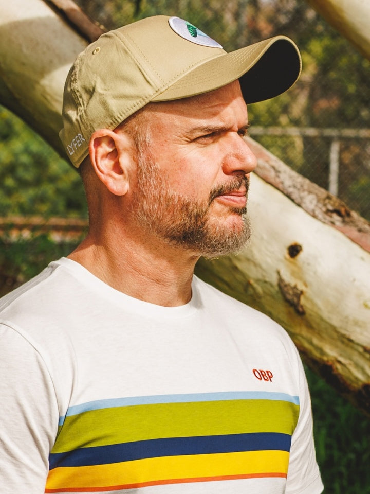 Model wearing a baseball cap outdoors, with a striped tshirt and a patch on the cap of a bird.