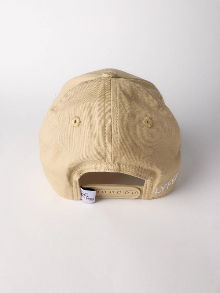 A beige baseball cap shown from the back, featuring a structured crown, ventilation eyelets, a plastic snapback closure, and partial white embroidered lettering on the side.