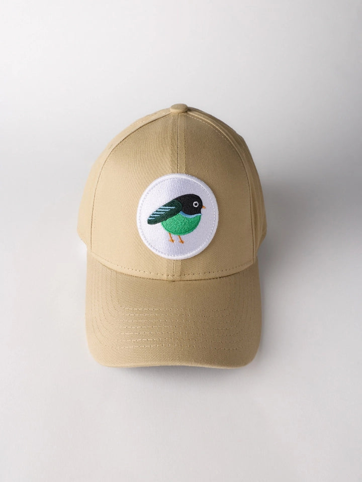 A beige baseball cap featuring a circular white patch on the front with an embroidered green and black bird, set against a plain light gray background.