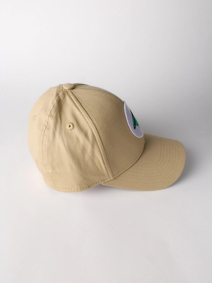 A beige baseball cap with a small circular patch on the side, photographed on a clean white studio background.