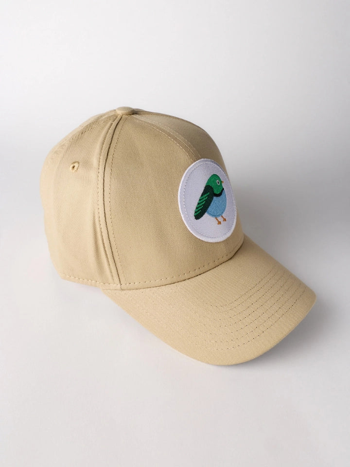 A beige baseball cap with a curved brim, featuring a circular white patch on the front with a colorful embroidered bird.