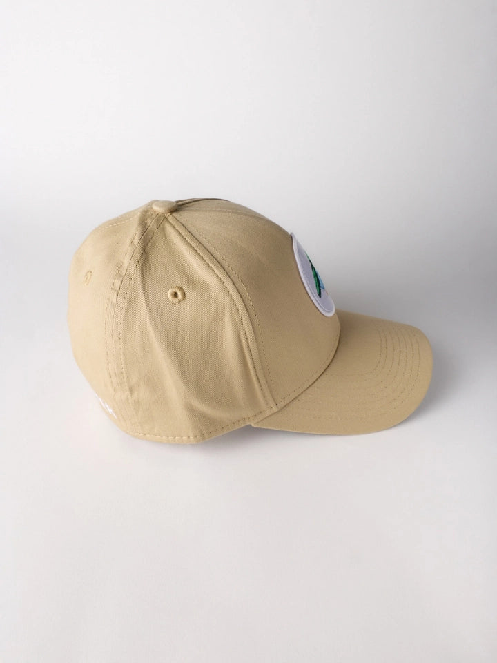 A khaki beige baseball cap with a small circular white patch on the side, photographed on a light gray studio background.