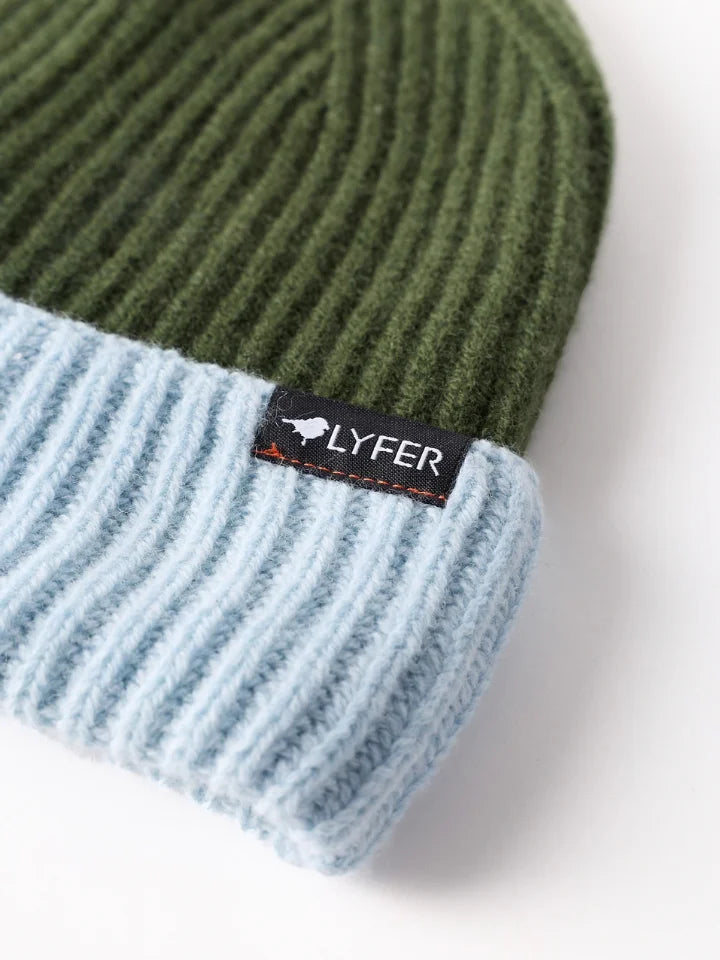 Close up a LYFER ribbed knit beanie hat with an olive green top section and a light blue folded cuff, featuring a small black brand LYFER tag on the side.